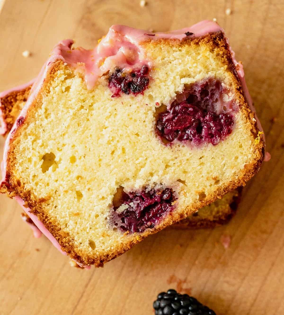 Top view of slice of lemon blackberry loaf cake on wooden surface.