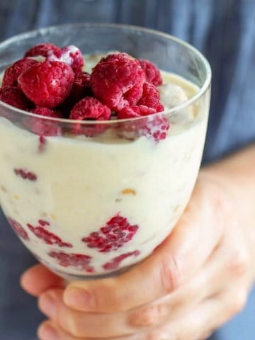 Close up of goblet with lemon and raspberry dessert being held with a blue shirt as background.