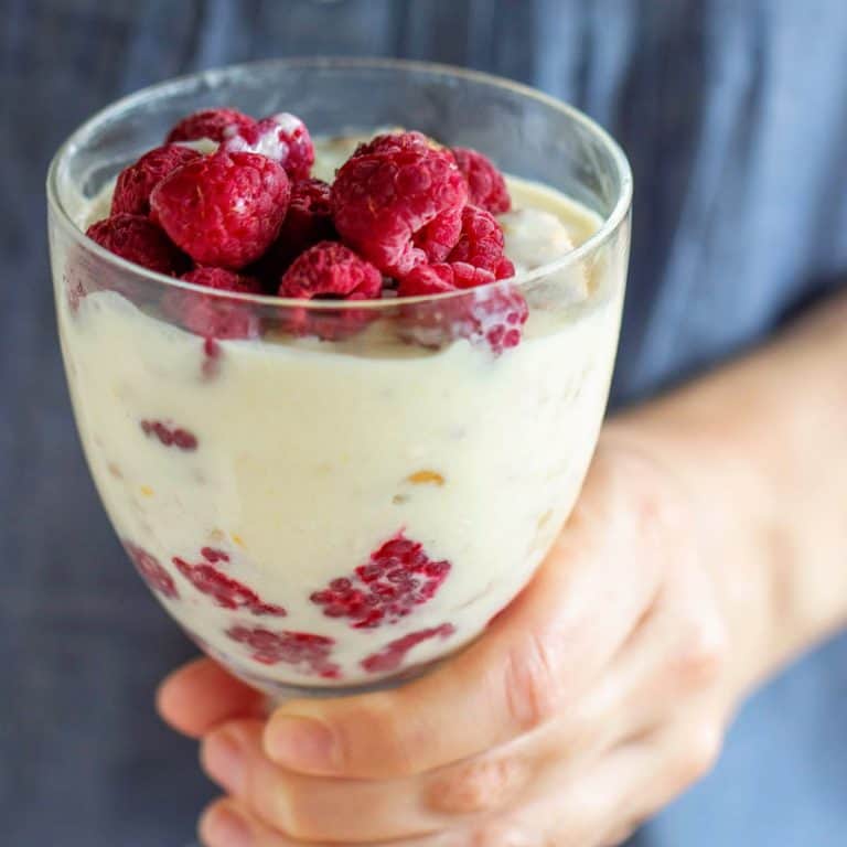 Close up of goblet with lemon and raspberry dessert being held with a blue shirt as background.