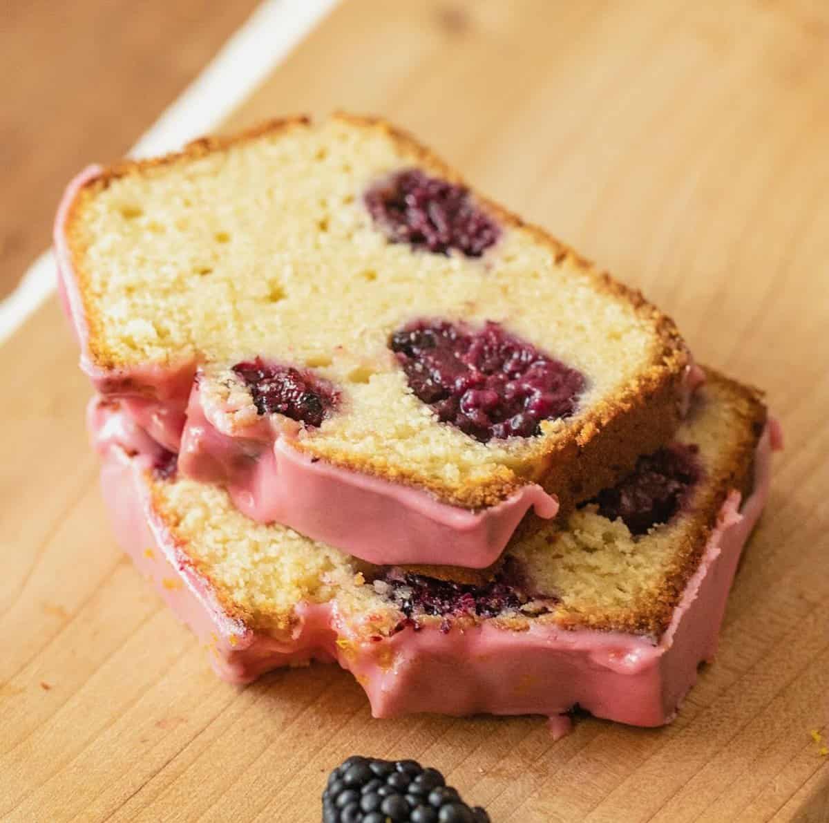 Two slices of blackberry bread with pink glaze on wooden board.
