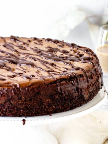 Partial view of whole chocolate cheesecake on a white cake stand and background. Glass with baileys.