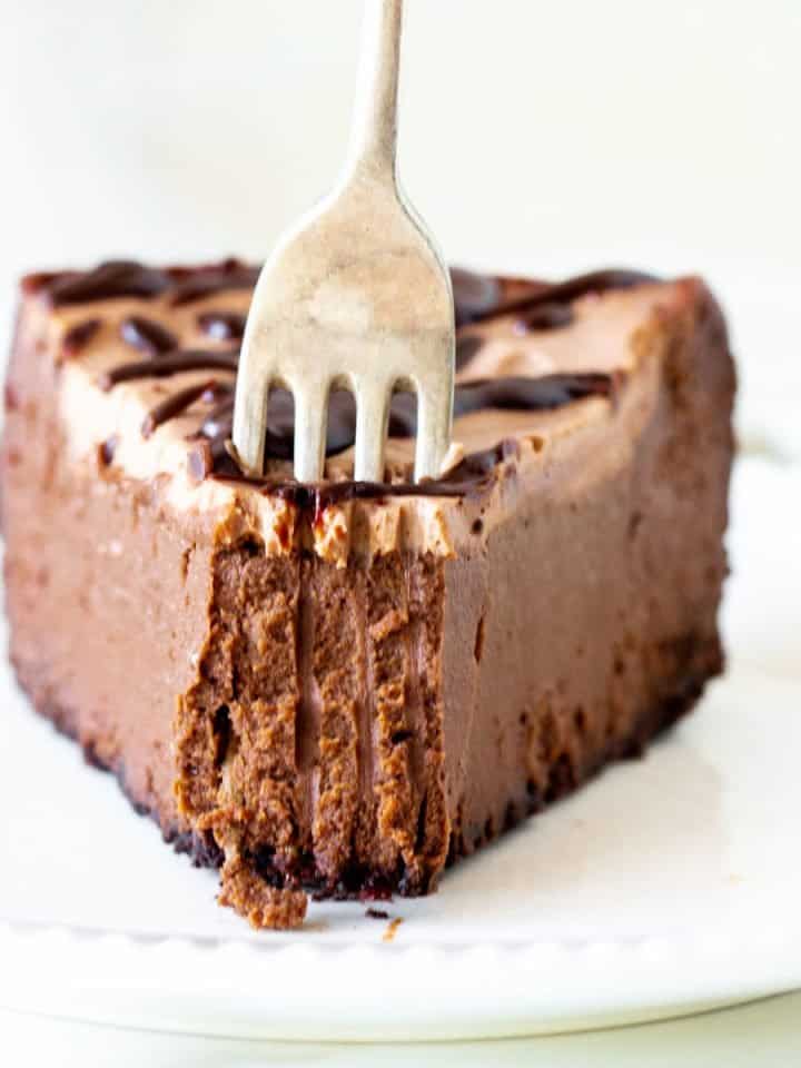 Silver fork inserted in a slice of chocolate cheesecake on a white plate.