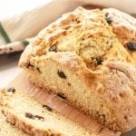 Baked Irish soda bread with raisins on a wooden board with kitchen towel in the background.