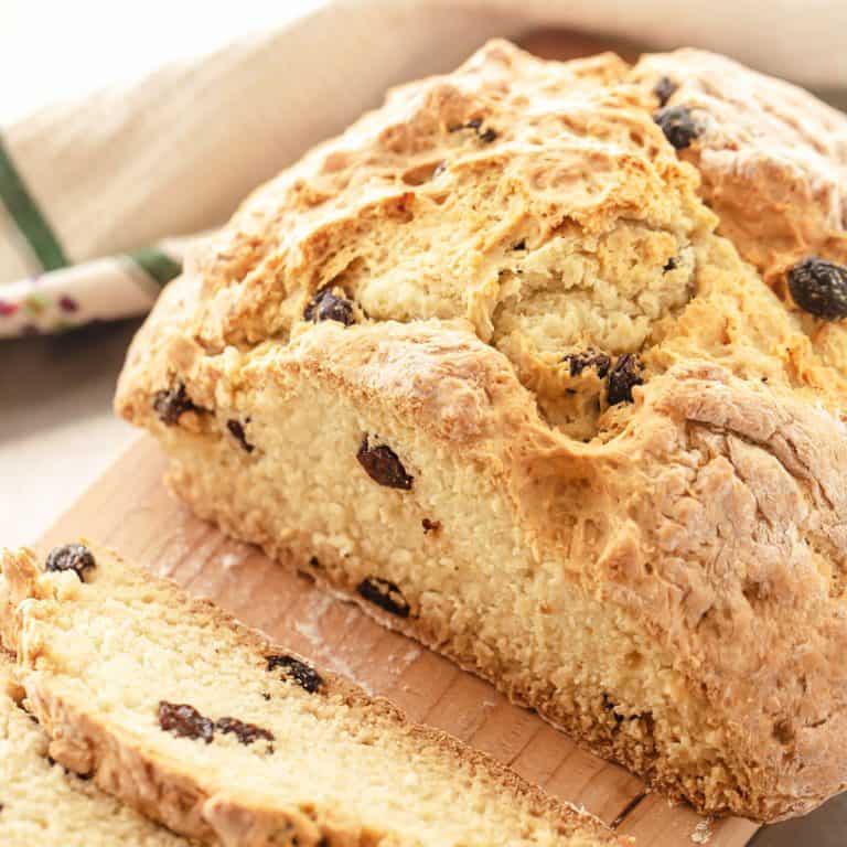 Baked Irish soda bread with raisins on a wooden board with kitchen towel in the background.