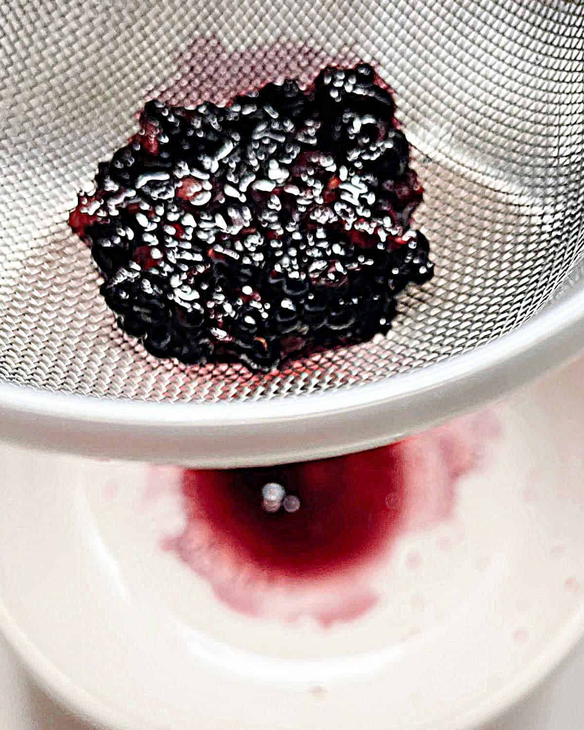 Colander with blackberry pulp over a white bowl with juice.