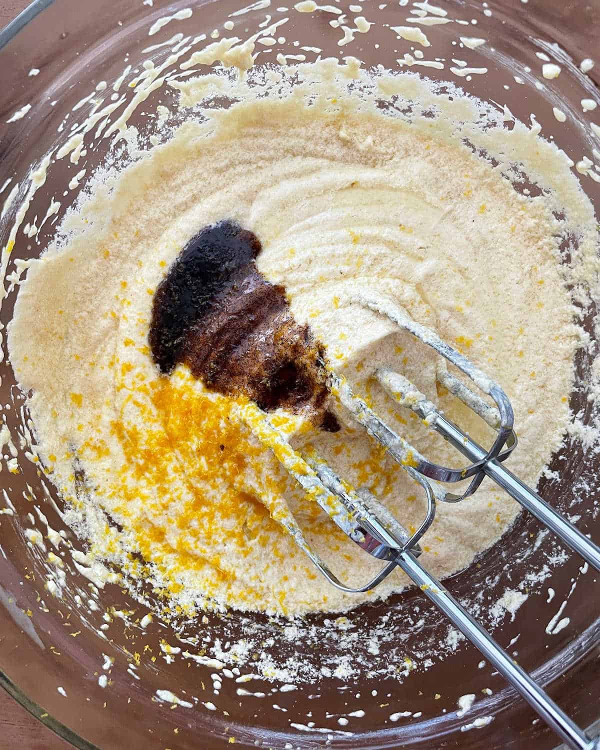 Vanilla and zest added to cake batter in a glass bowl on a wooden surface. 
