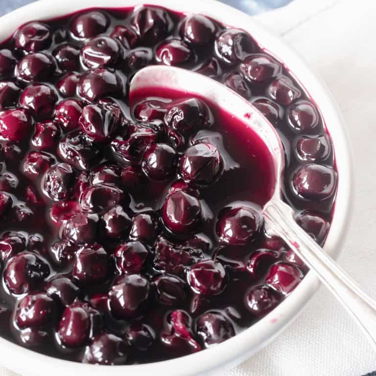 Very close up image of blueberry compote in white bowl with silver spoon.