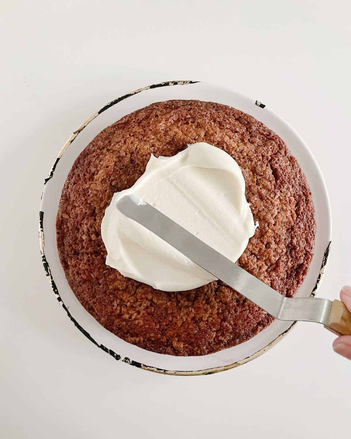 Filling a carrot cake layer with cream cheese frosting and an offset spatula. White surface.