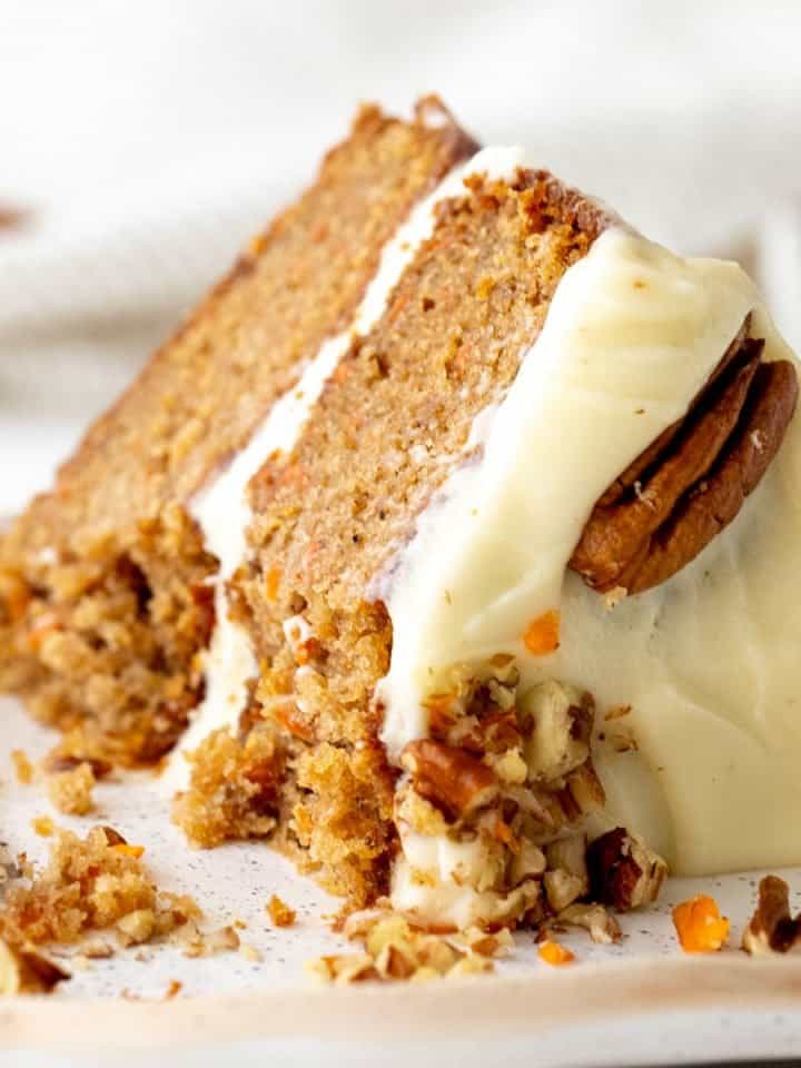 Close up of eaten slice of frosted carrot cake on white plate and background.