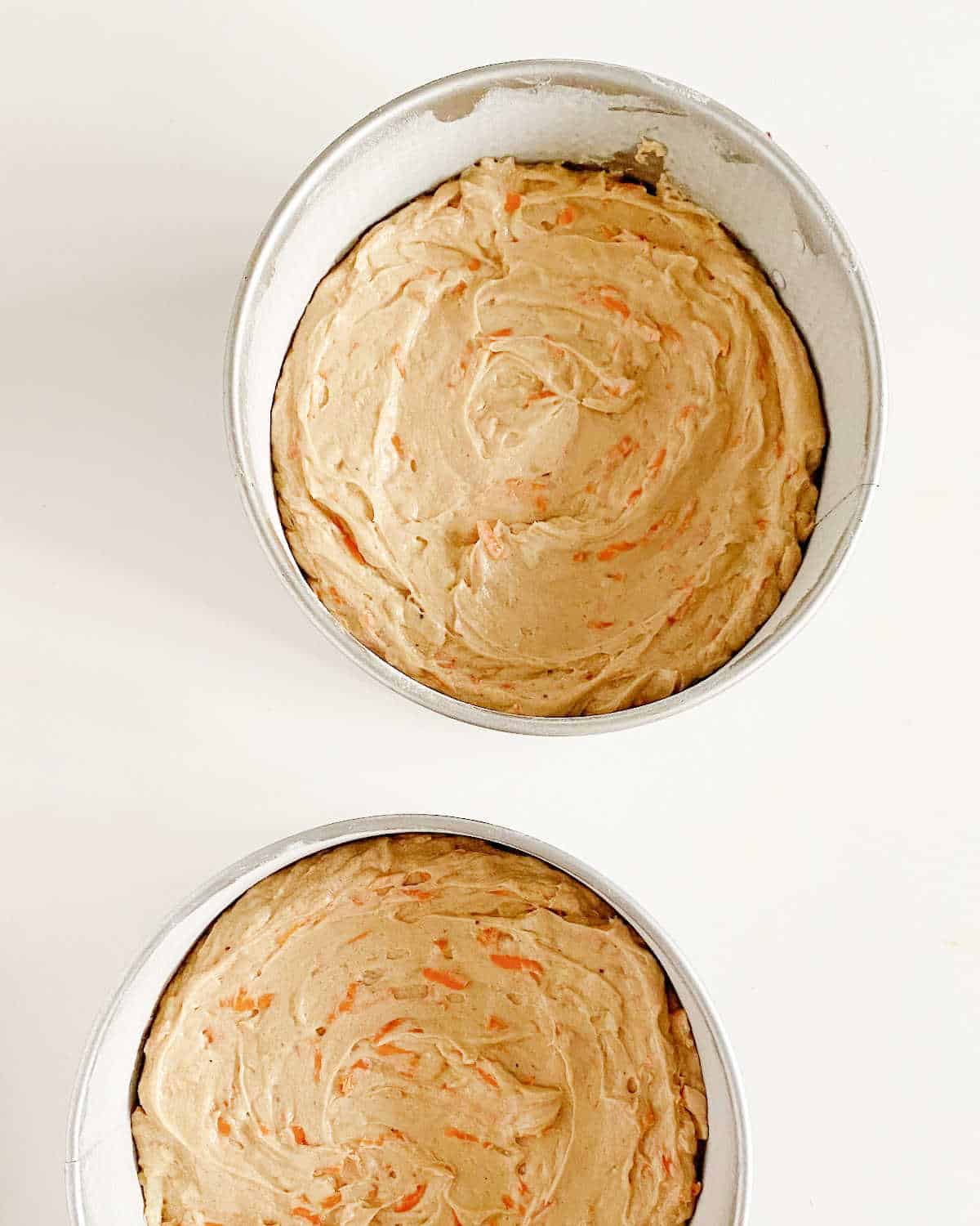 Unbaked carrot cake batter in round cake pans on a white surface.