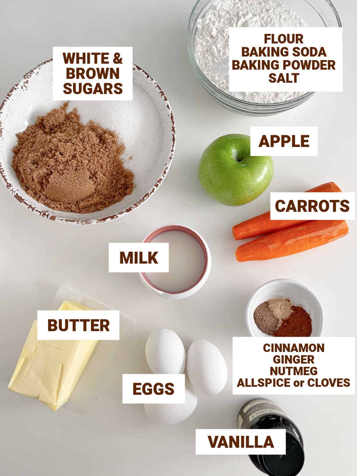 Carrot cake ingredients on white surface, including apple, sugar, butter, vanilla, spices, milk; text overlay.