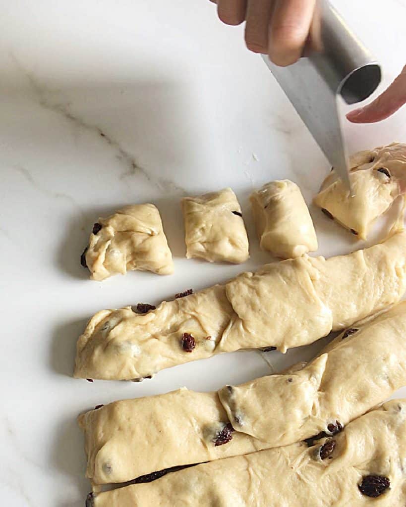 Cutting strips and pieces of hot cross buns dough on a white marble surface.
