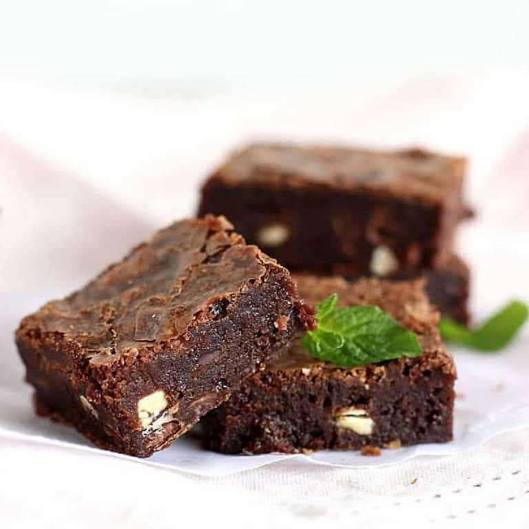 Two stacked brownies and one on background on pinkish cloth with mint leaves.