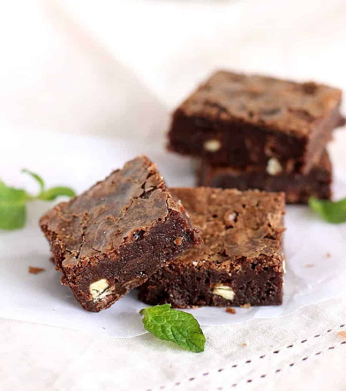 Scattered brownie squares on pinkish linen with mint leaves around. 