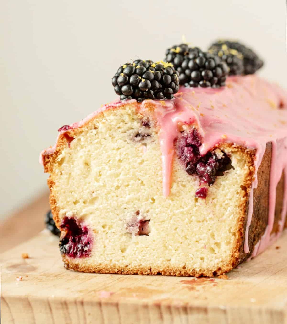 Dripping pink glaze on loaf of cut blackberry lemon bread on a wooden board.