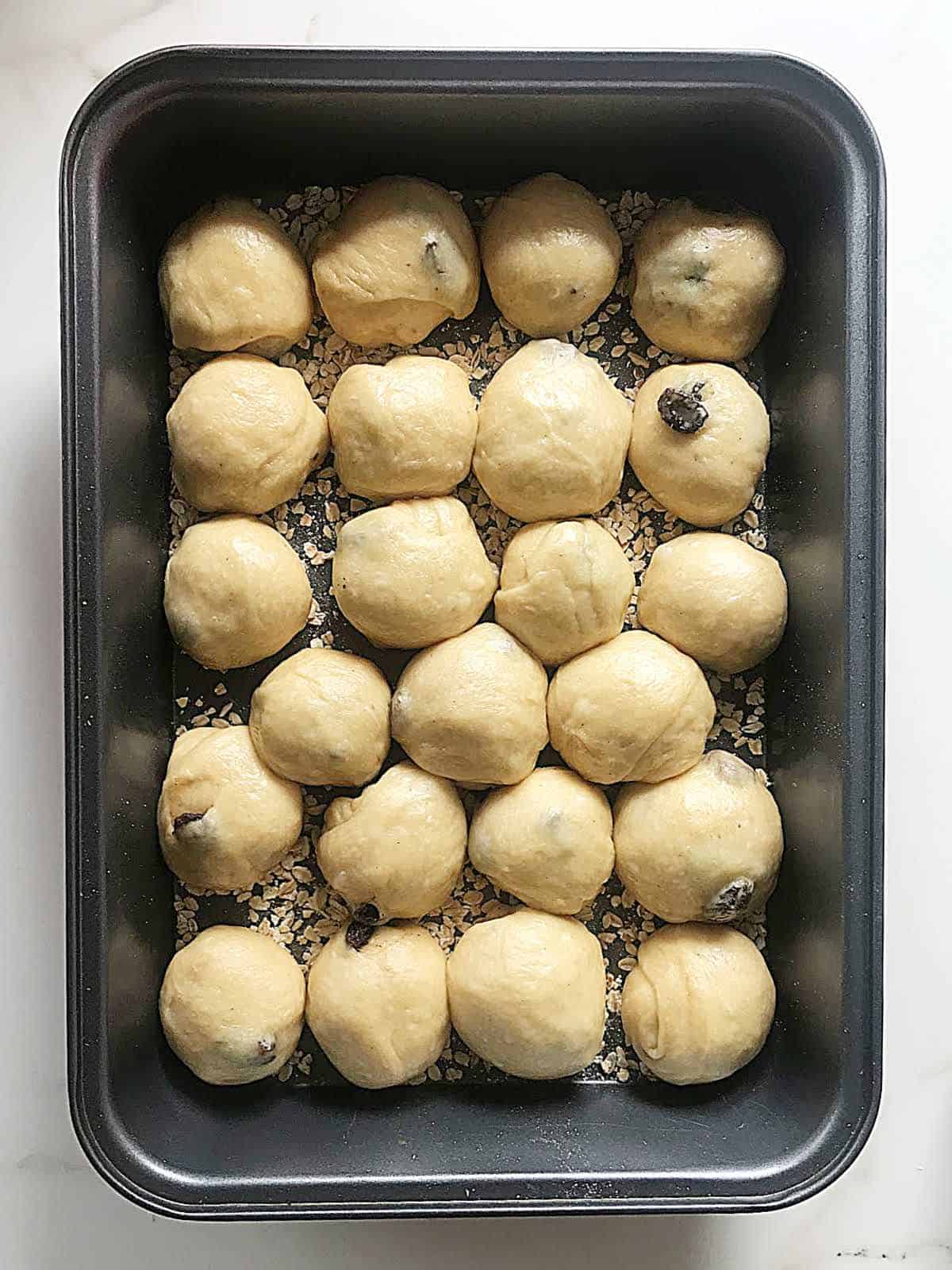 Small buns in rows in a rectangular metal pan before rising.