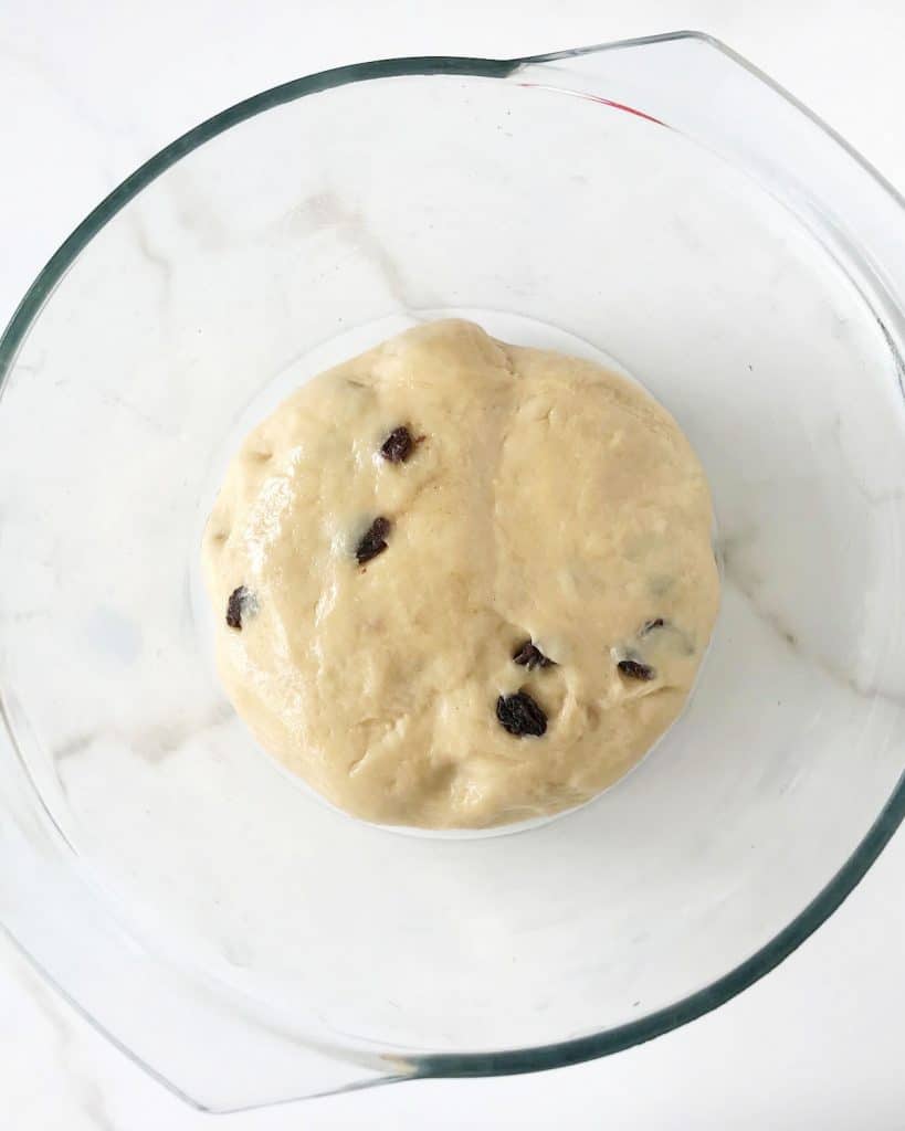 Glass bowl with bread dough with raisins. White marble surface.