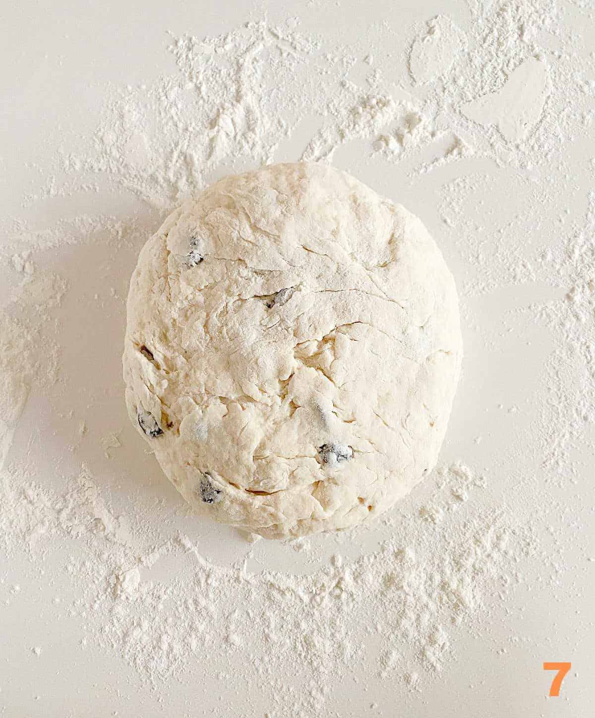 Ball of raisin soda bread on floured white counter.