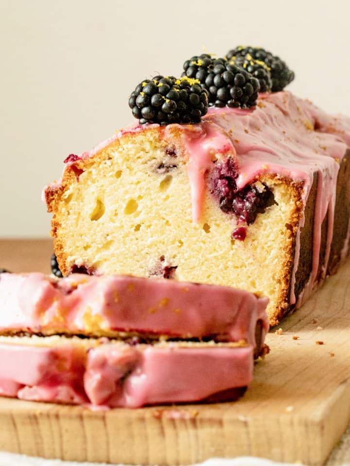 Close up of blackberry bread with pink icing on wooden board, cut slices in front.