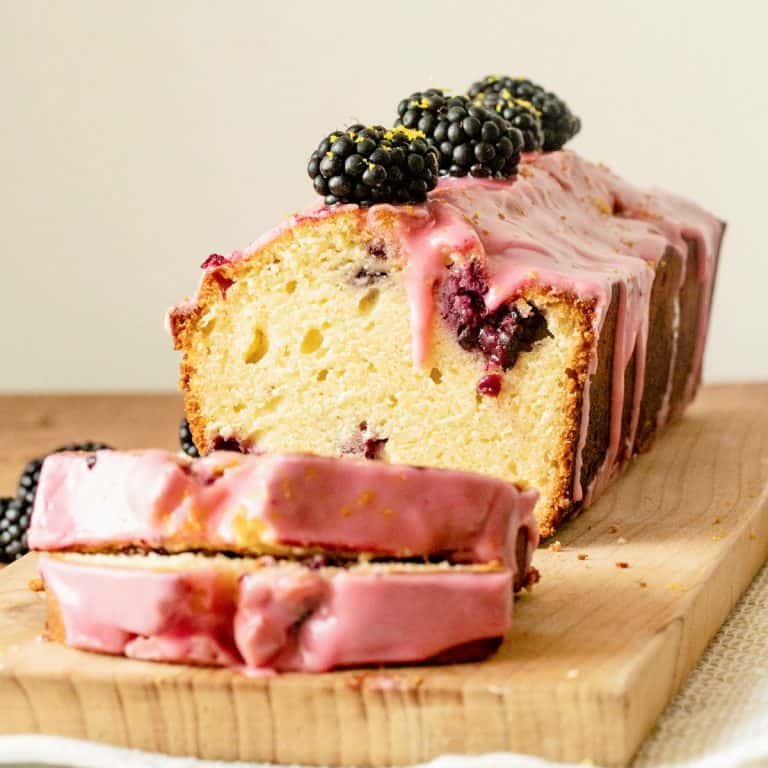 Close up of blackberry bread with pink icing on wooden board, cut slices in front.