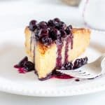 Single slice of lemon cake with blueberry sauce on white plate, silver fork, white background.