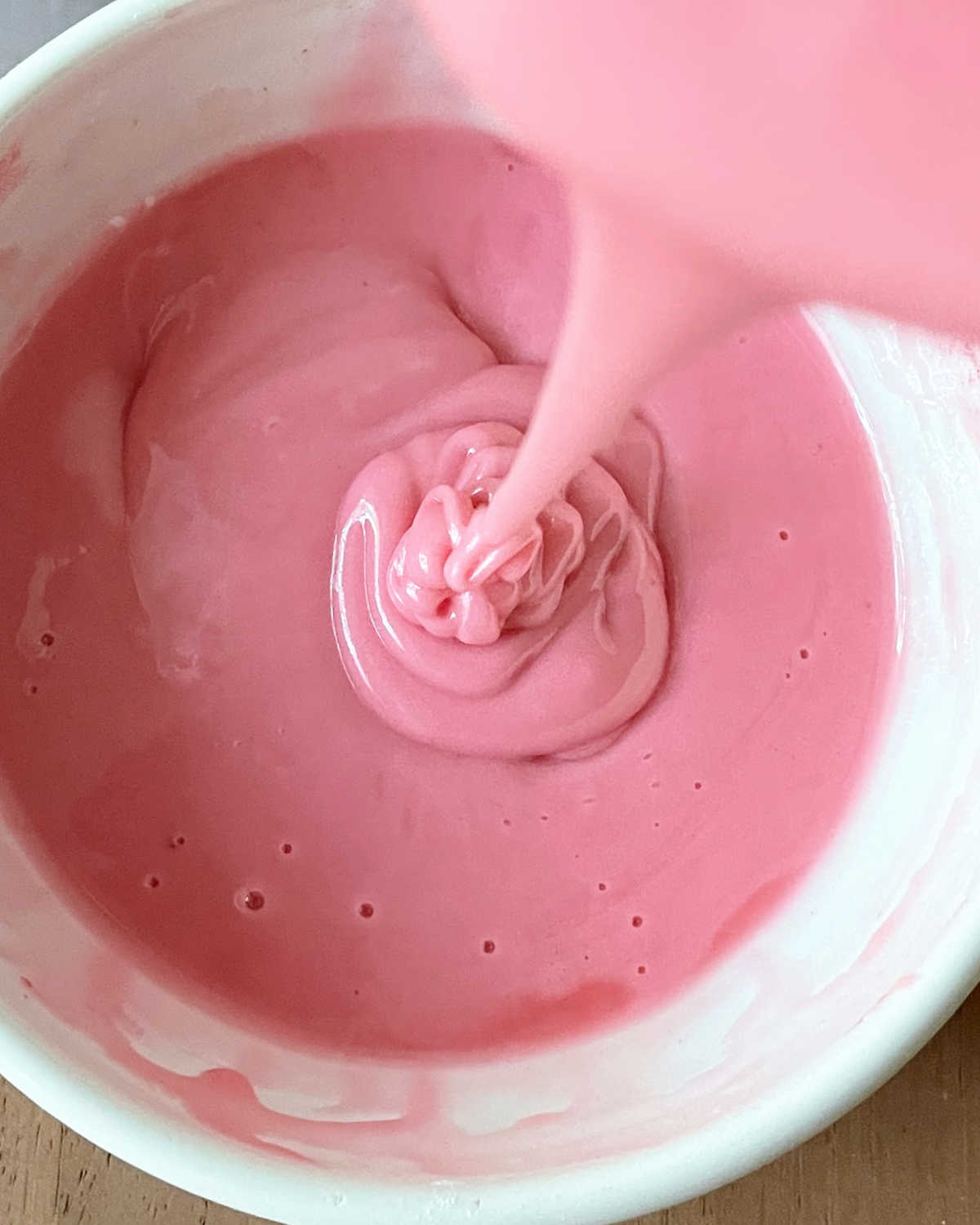 Pink glaze being poured in a white bowl.