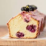 Cut glazed blackberry bread on wooden board, beige background.