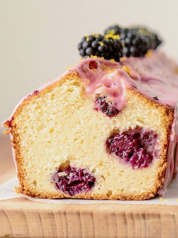 Cut glazed blackberry bread on wooden board, beige background.