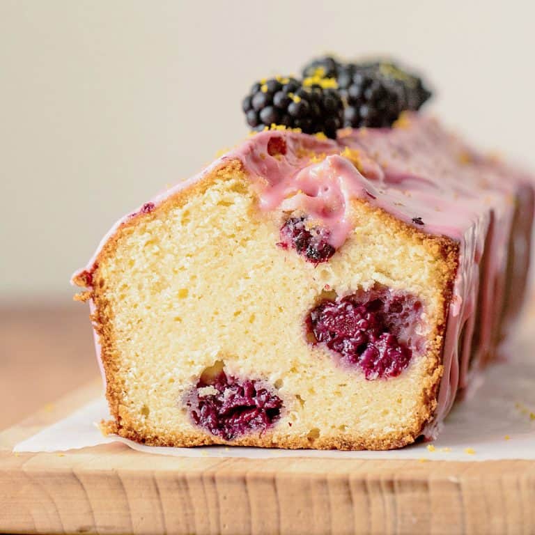 Cut glazed blackberry bread on wooden board, beige background.