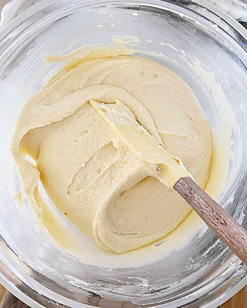 Yellow spatula folding lemon cake batter in glass bowl.