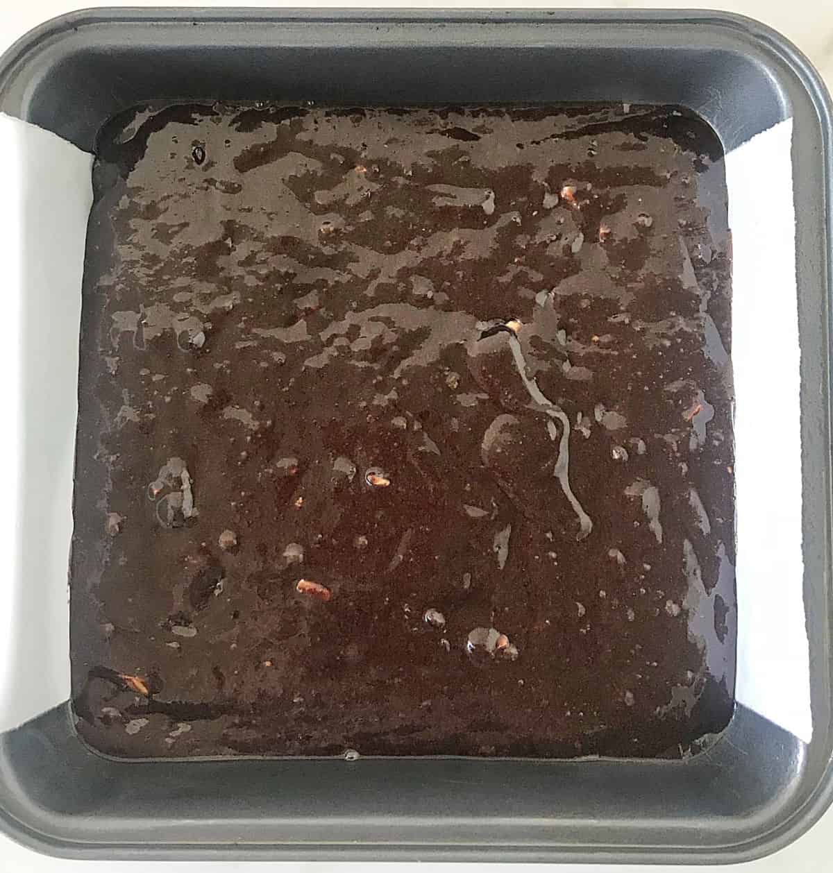 Unbaked brownie batter in metal square pan with parchment paper.