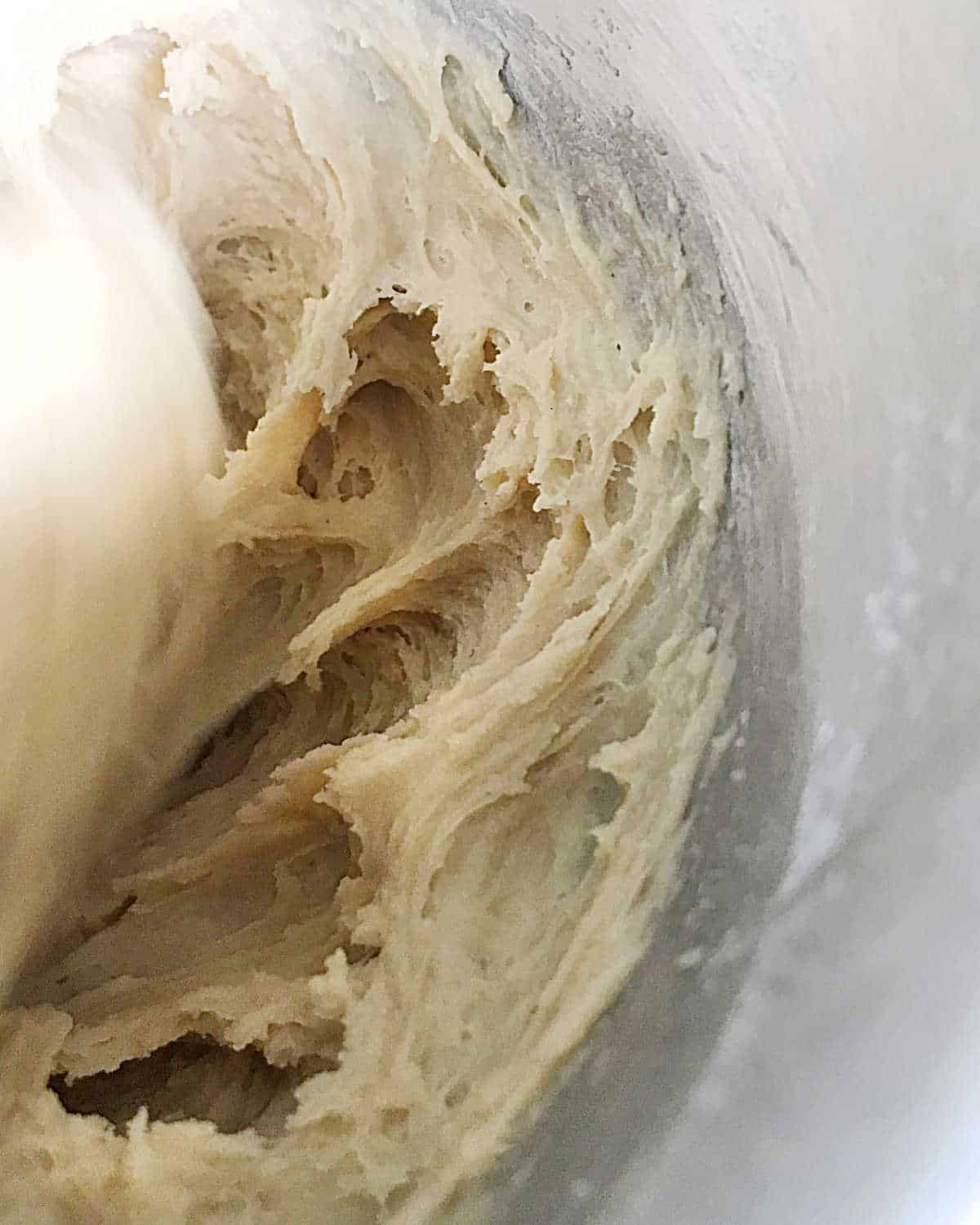 Sweet buns dough being mixed in a metal bowl of a stand mixer. Close up image.