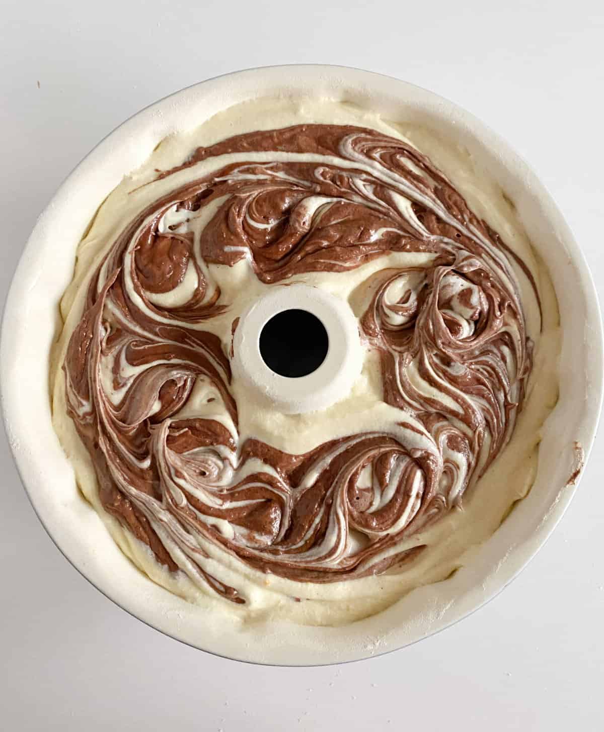 Top view of white and brown marbled unbaked bundt cake in white pan on white surface.