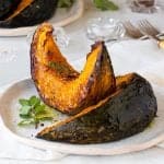 White plate with two wedges of roasted pumpkin, white background, herbs, forks, salt.