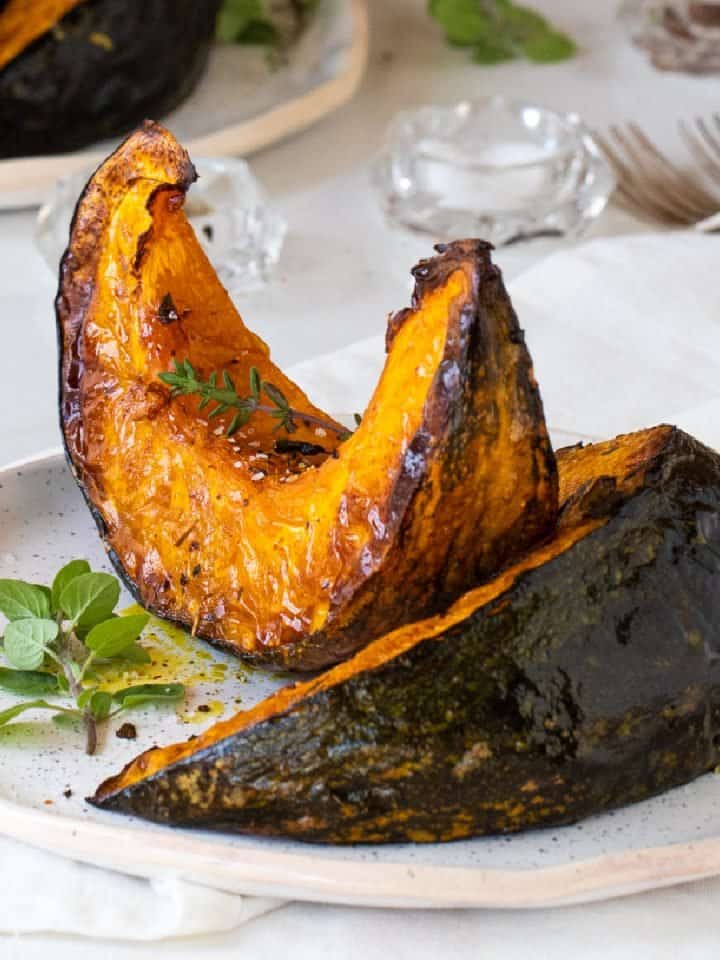 White plate with two wedges of roasted pumpkin, white background, herbs, forks, salt.