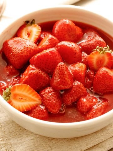 Top view of white bowl with strawberry compote on beige napkin.