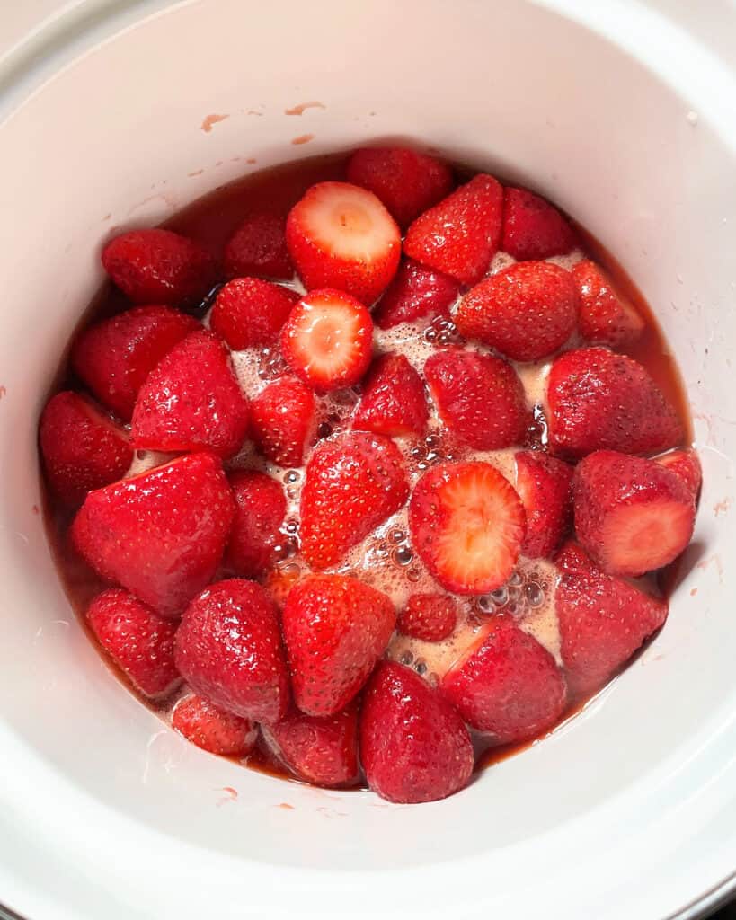 Simmering strawberries and juices in a white saucepan.