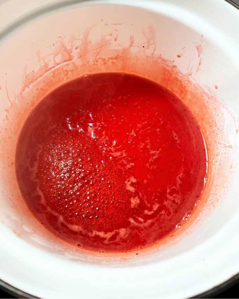 White saucepan with simmering strawberry juice.