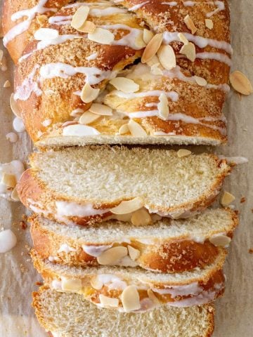 Beige parchment paper with sliced glazed almond Easter braided bread. Top partial view.