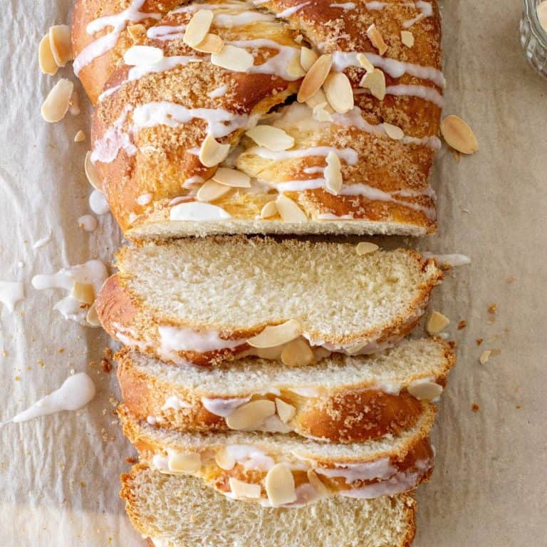 Beige parchment paper with sliced glazed almond Easter braided bread. Top partial view.