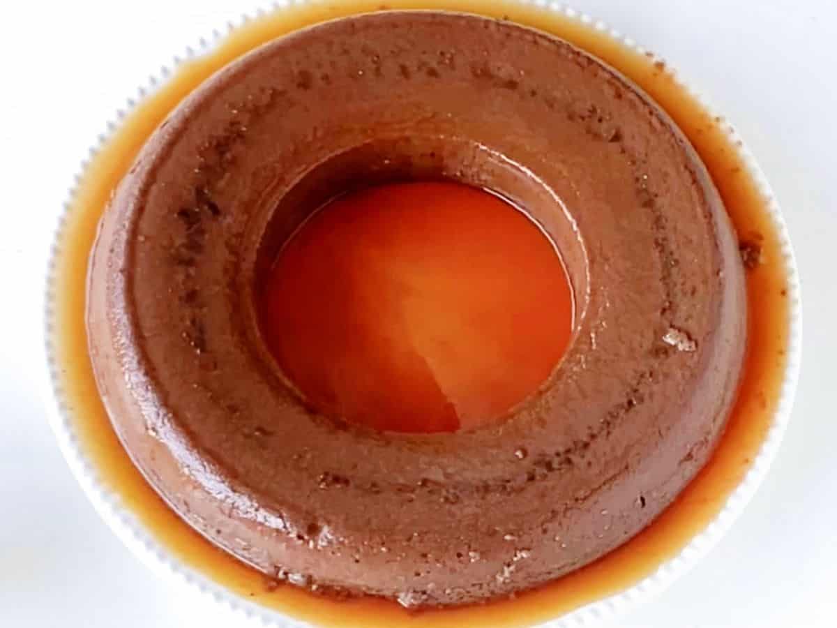 Whole baked cchocolate flan on white plate, close up view.
