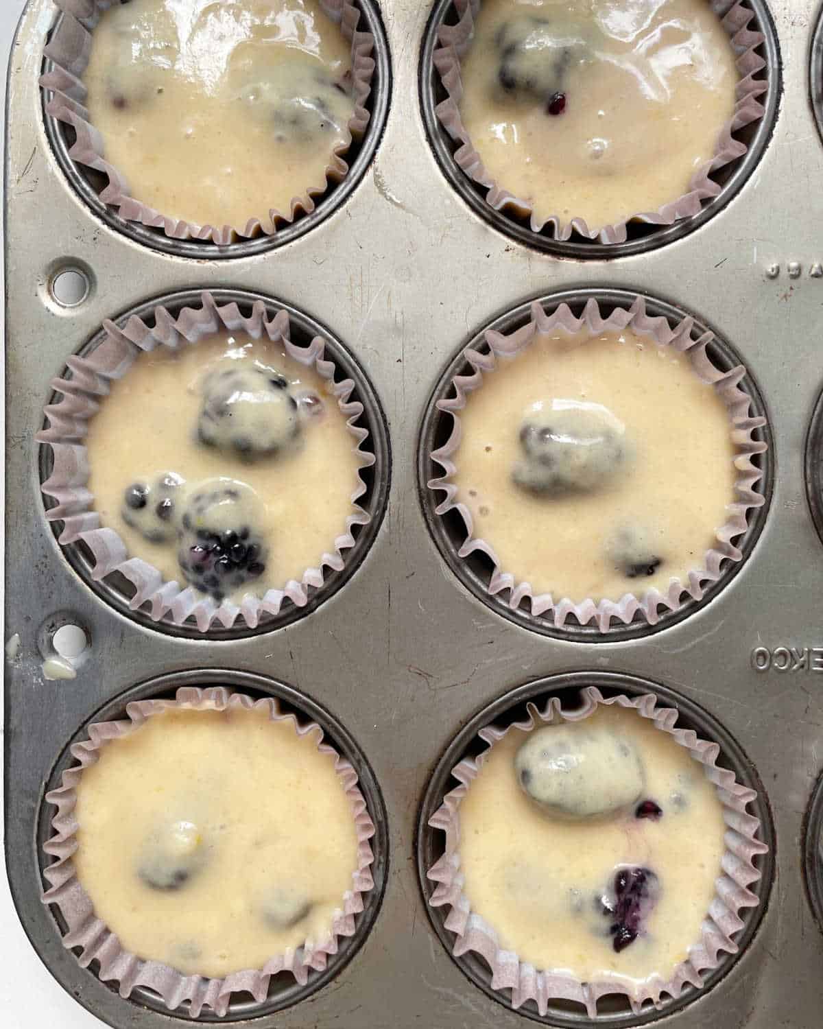 Close up image of muffin liners in a metal pan with blackberry muffin batter.