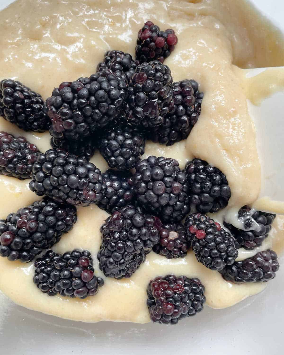 Fresh blackberries added to muffin batter in a glass bowl.