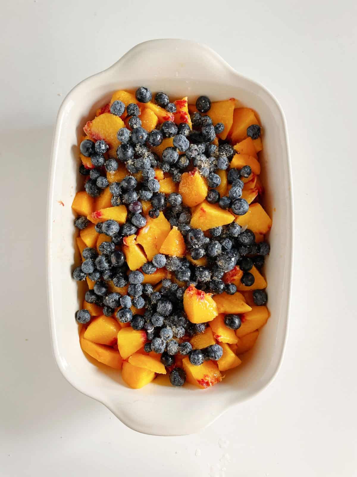 Peaches and blueberries in whitish rectangular ceramic dish on a white surface.