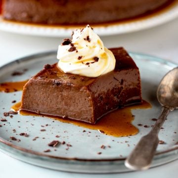 Grey plate with single serving of chocolate flan with dollop of cream and a silver spoon.