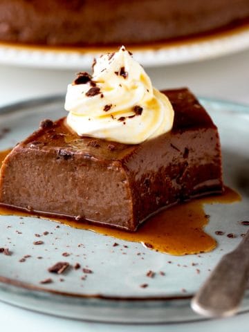 Grey plate with single serving of chocolate flan with dollop of cream and a silver spoon.