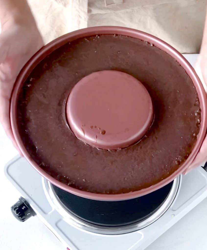 Baked chocolate flan in the pan being held over single electric stove.