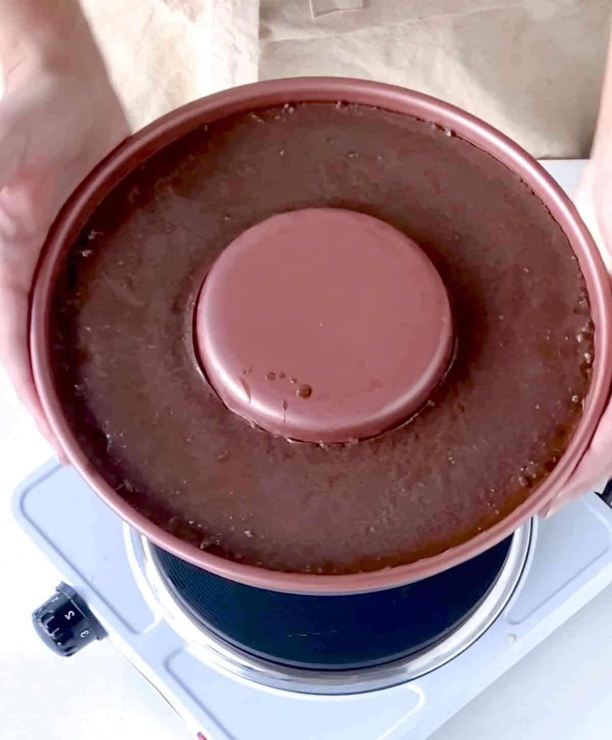 Baked chocolate flan in pan being held over single electric stove.