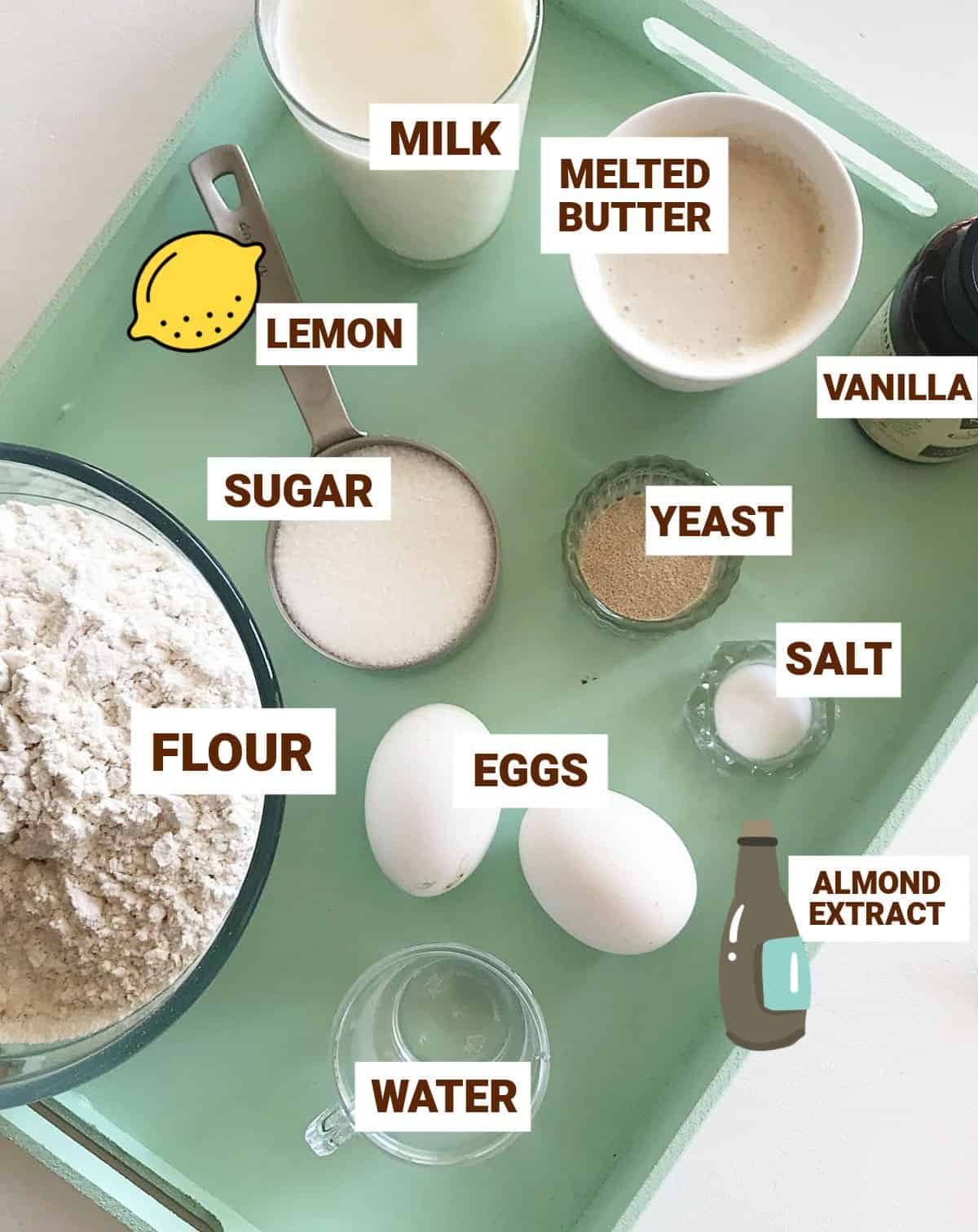 Green tray with bowls of ingredients including flour, milk, sugar, eggs, yeast, lemon, vanilla, butter.