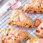 Overview of glazed strawberry scones on metal wire rack.